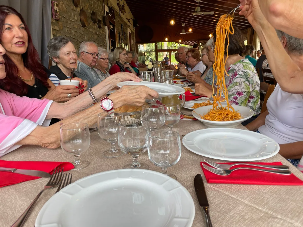 Menschen sitzen an einem Tisch und schöpfen Pasta,